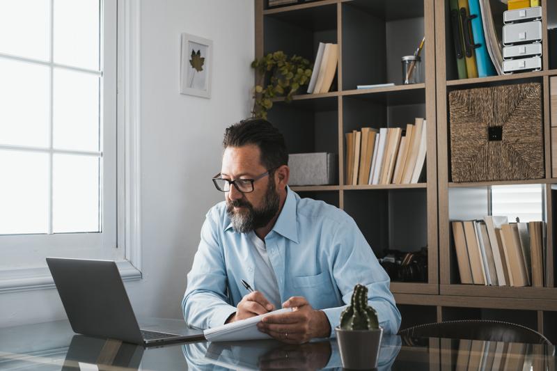 Happy young caucasian businessman smiling working online watching webinar podcast on laptop and learning education course conference calling make notes sit at work desk, elearning concept