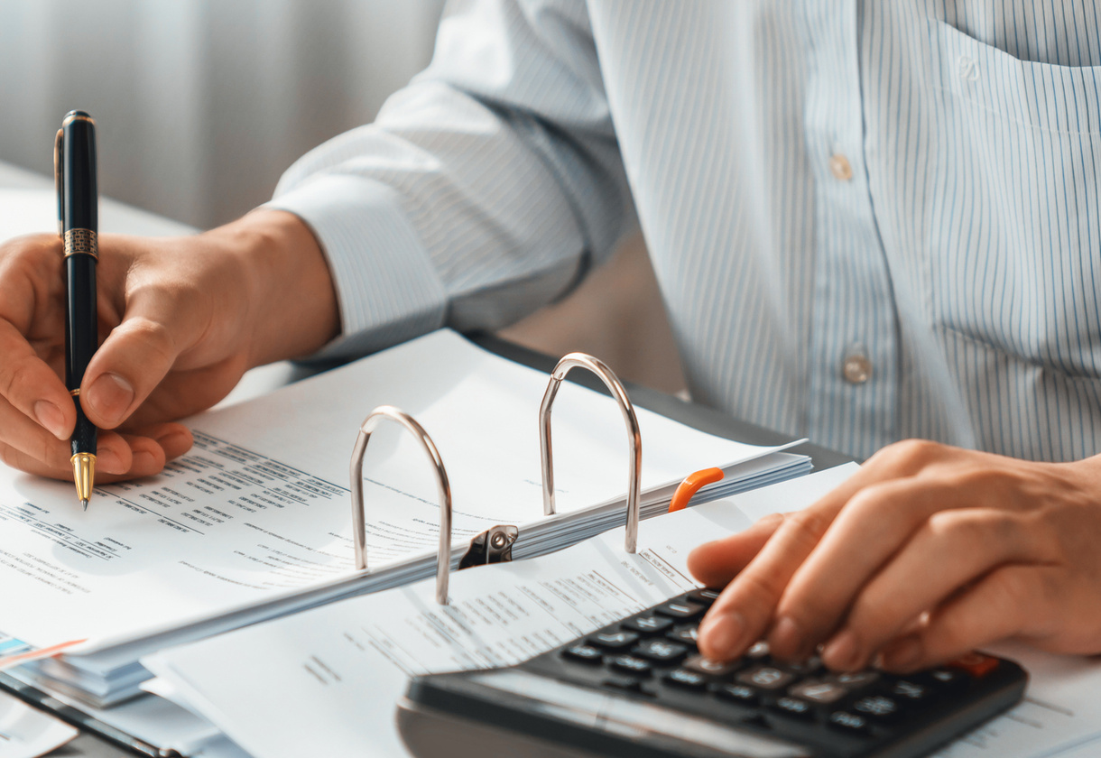 Corporate auditor calculating budget with calculator on his office desk. Dedicated accountant professional of accounting business company analyzing financial document to forecast income. Insight