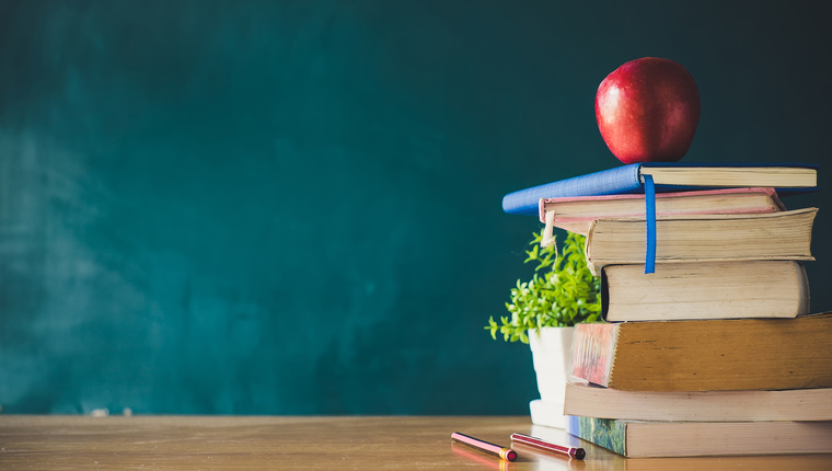 School books with red apple on desk over green school board background