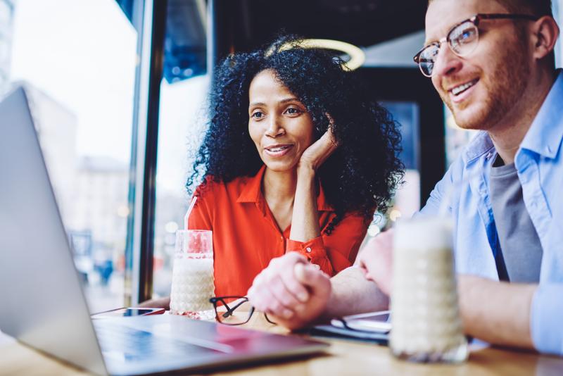Happy diverse male and female friends watching motivation webinar via app on modern laptop togetherness while spending leisure in cafe interior, cheerful hipster guys enjoying online video chat